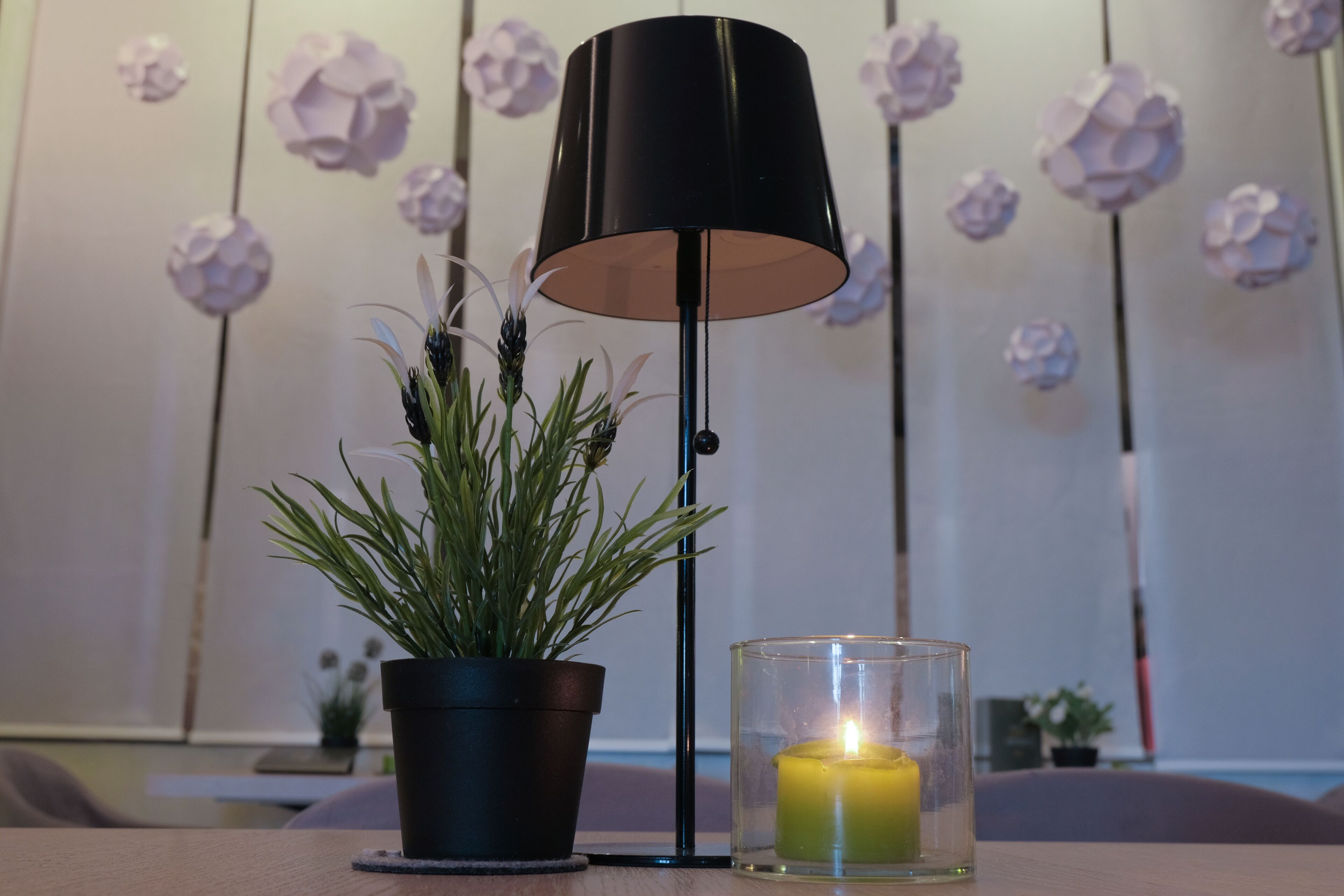 A room with a black floor lamp, a potted plant, and a lit candle on a table.