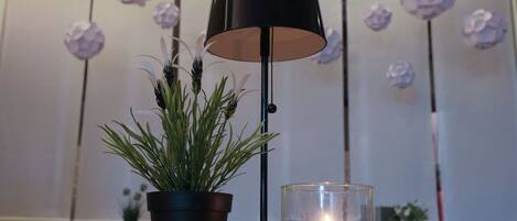 A room with a black floor lamp, a potted plant, and a lit candle on a table.
