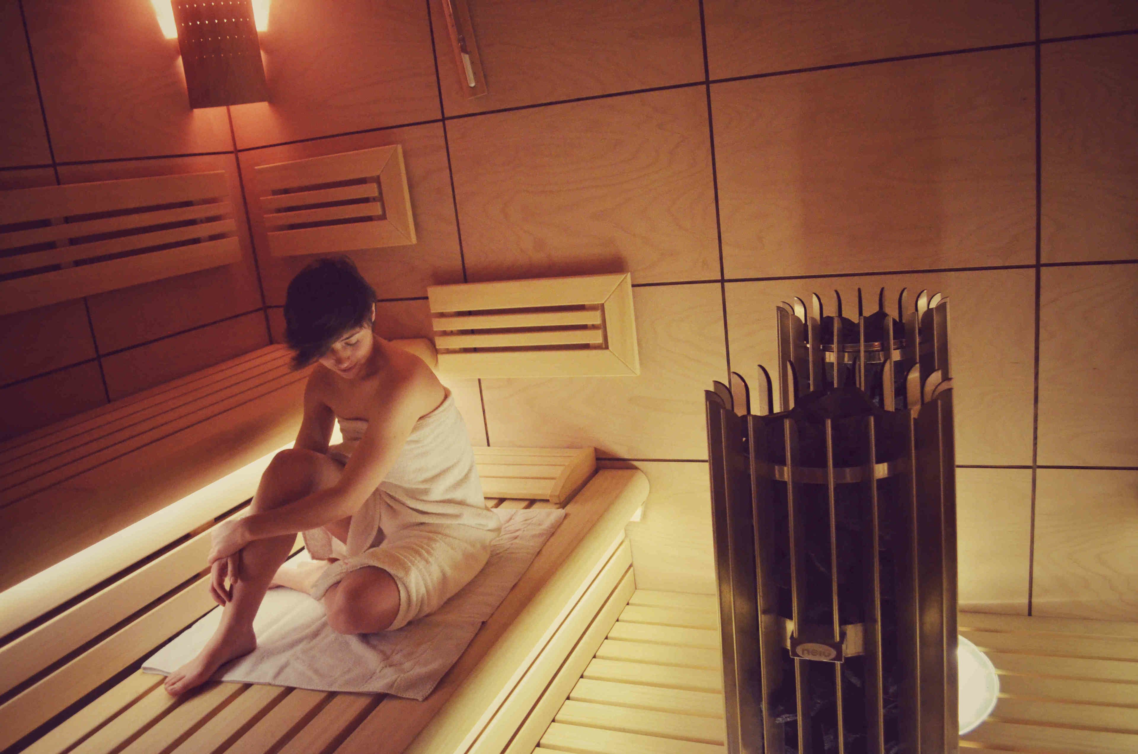 A person sitting on a bench in a room with wooden benches and a sauna.