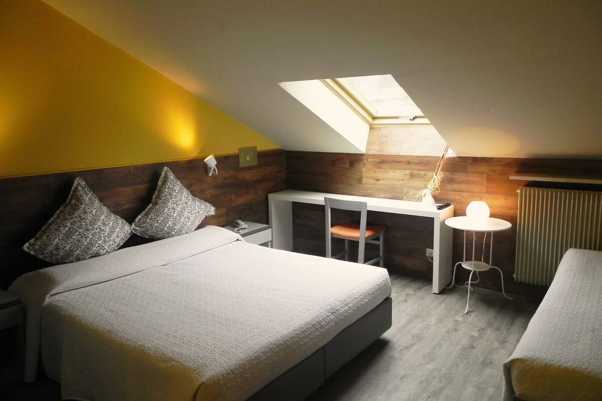 A modern bedroom with a bed, a desk, and a chair. There is a skylight above the desk.