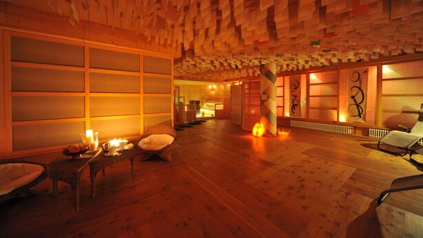 A room with wooden flooring, a low ceiling with paper-like decorations, and a seating area with cushions and a table with candles. - Liberty (Levico Terme)