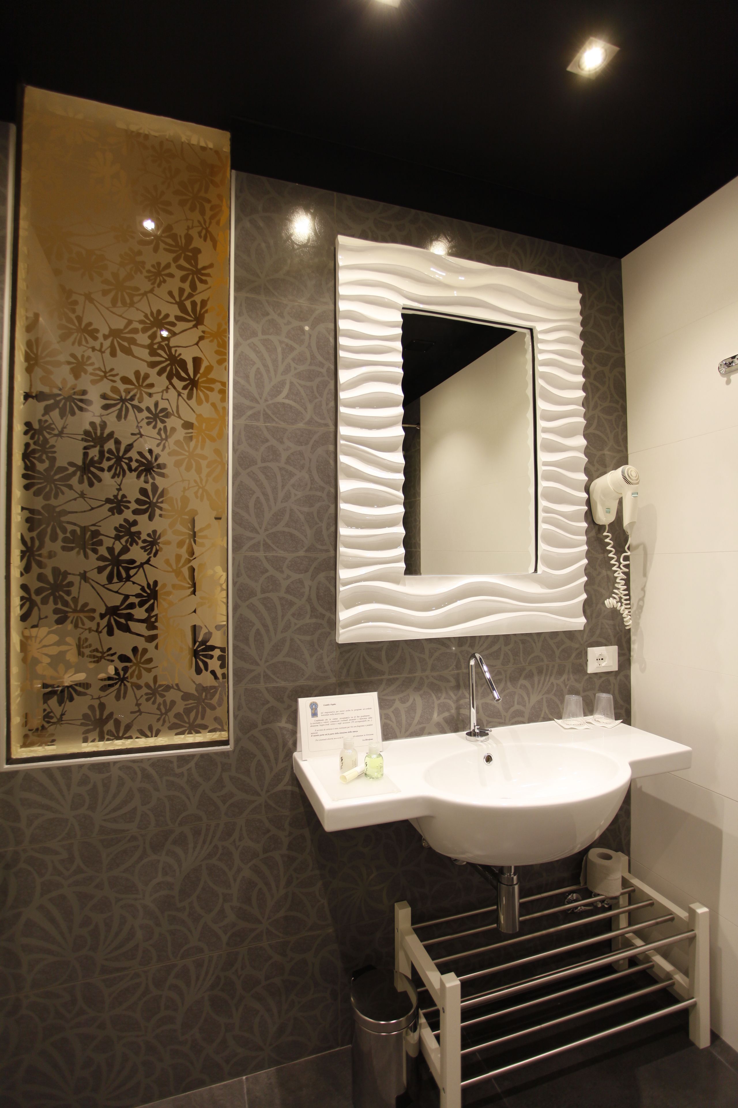 A modern bathroom with a large mirror, a sink, and a hairdryer mounted on the wall.