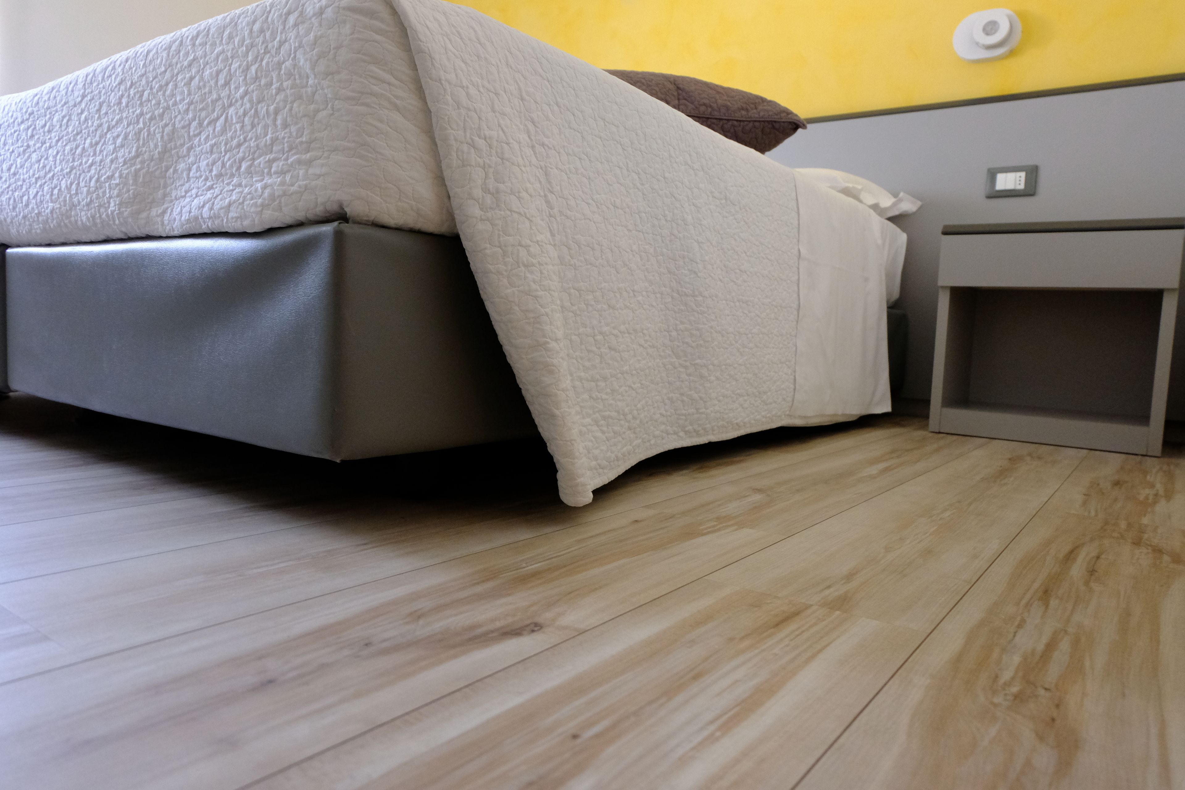 Una cama con cubre cama blanco, una mesita de noche y un pequeño armario.