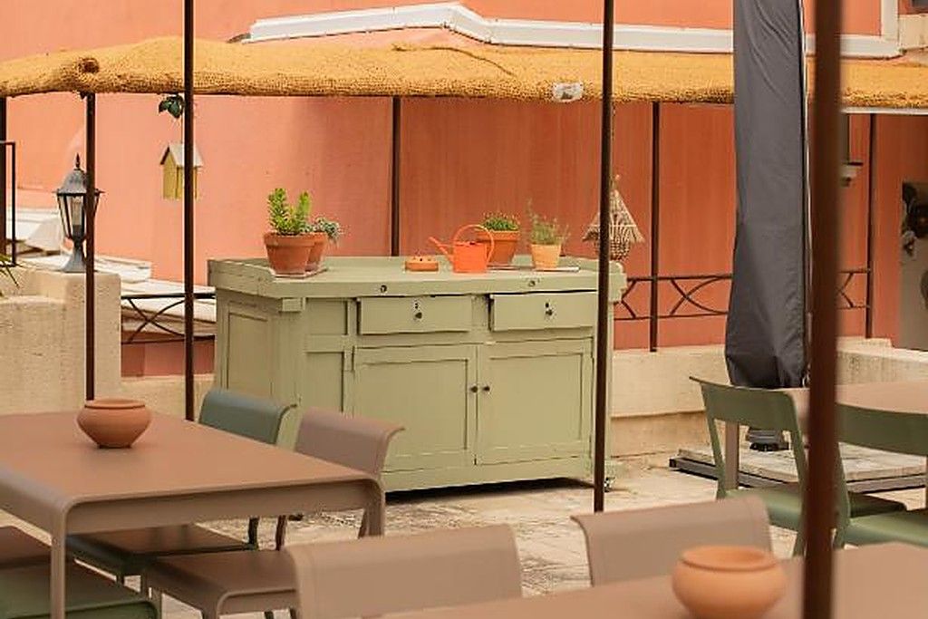 Un espace extérieur aménagé avec des tables et des chaises, un meuble vert contenant des plantes en pot et un parasol jaune.