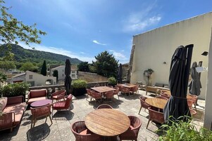 Un patio exterior con mesas redondas y sillas de mimbre, rodeado por un muro bajo y plantas en macetas.