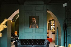 Una habitación con un sofá de color oscuro, un cuadro en la pared y un arco que da a otra estancia.