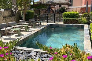 Una piscina con borde de piedra, rodeada de mobiliario exterior y un muro de piedra.