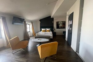 Una habitación de hotel moderna con una cama, dos sillas, una mesa redonda pequeña y un cuadro grande en la pared.