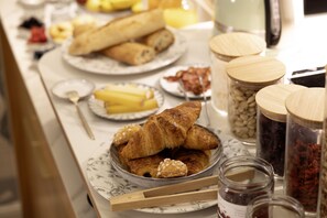 A breakfast buffet with croissants, pastries, and various food items on a marble table. - Hôtel L de Lutèce - Notre-Dame (Paris)