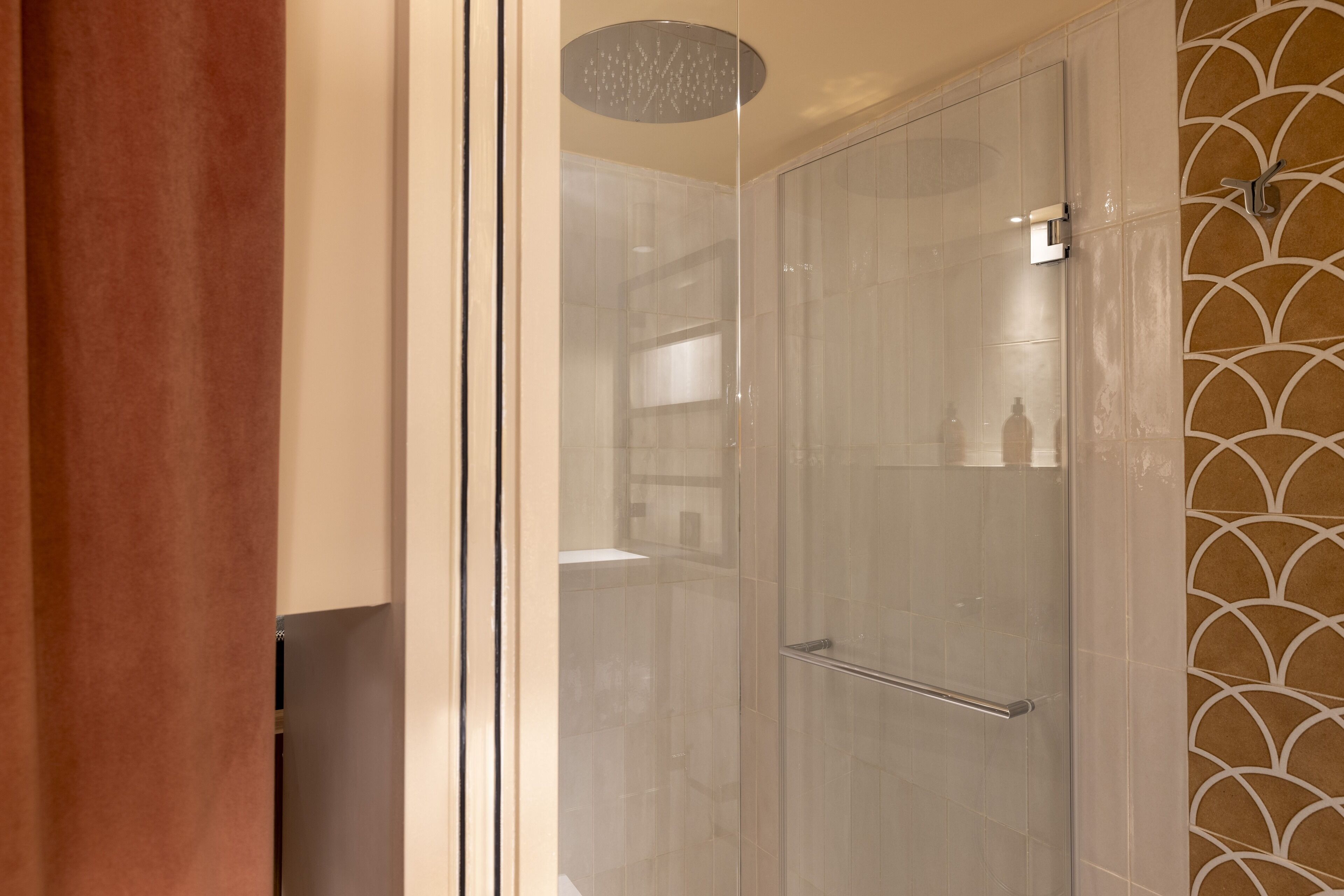 Un baño moderno con ducha envuelta en vidrio, pared de azulejos blancos y diseño de baldosas estampado a la derecha.