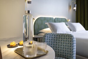 A hotel room with a bed, a chair, a tray with glasses and a bottle, and a wall-mounted lamp. - Hôtel L de Lutèce - Notre-Dame (Paris)