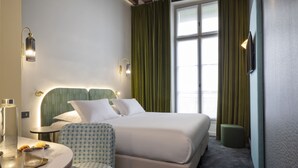 Una habitación de hotel con una cama, una silla, una mesa con lámpara y una ventana con cortinas.