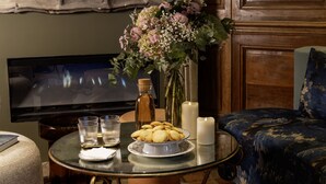 Una mesa redonda de vidrio con un plato de galletas, dos vasos, una vela y un jarrón de flores.
