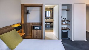 A hotel room with a bed, a desk with a computer, a small safe, and a walk-in closet.
