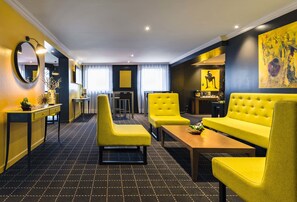 A modern living room with yellow sofas and armchairs, a coffee table, and a dining area with a small table and chairs.