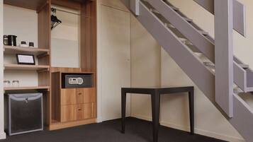 Una habitación moderna con un armario de madera, una pequeña mesa, una maleta gris y una escalera.