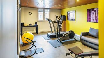 Ein Heimfitnessraum mit Trainingsgeräten, einer Couch und einem Fenster mit Jalousien.