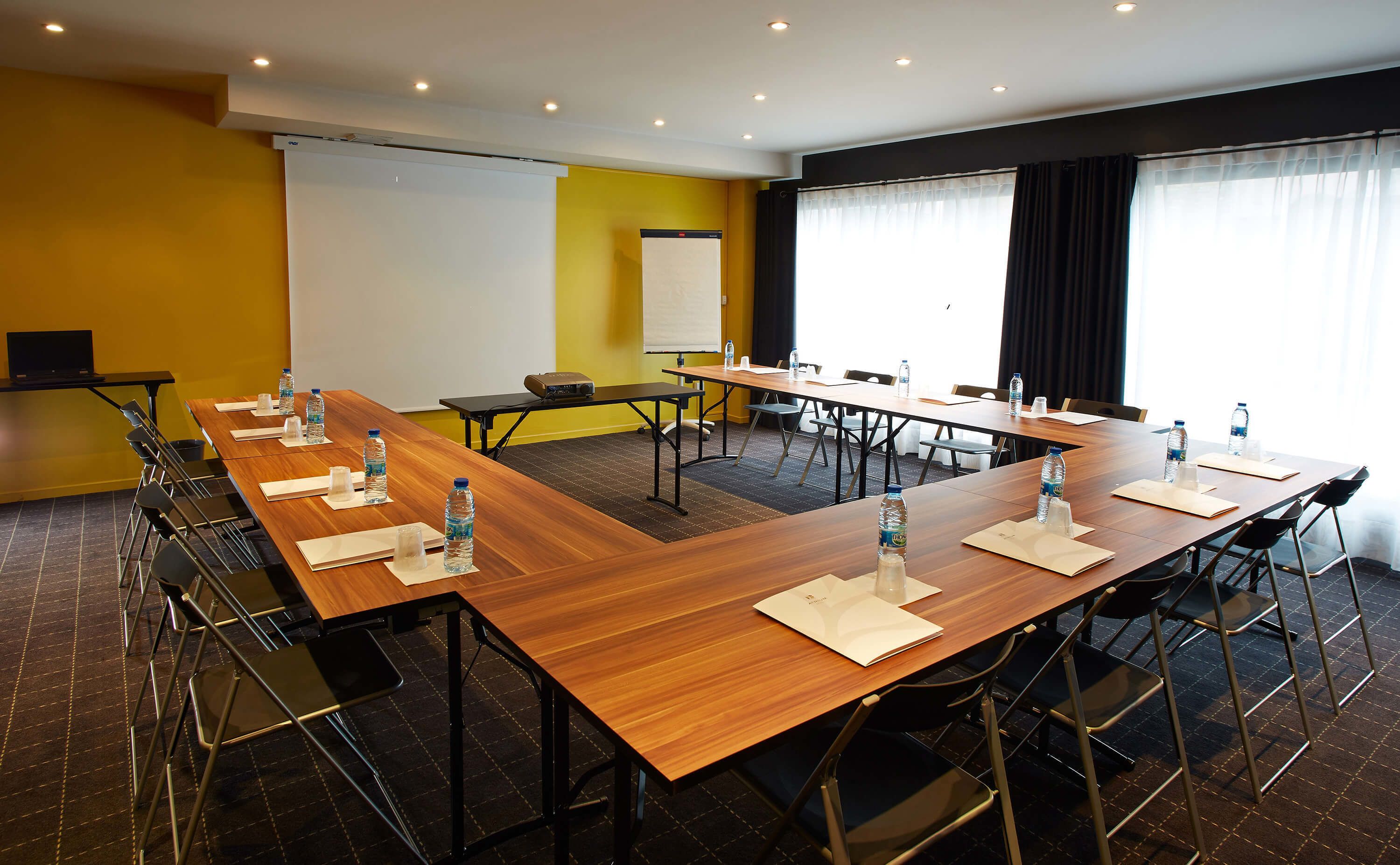 Ein Konferenzraum mit mehreren Tischen und Stühlen, ausgestattet mit Wasserflaschen und einer Projektionsleinwand.