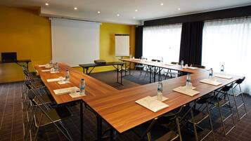 Ein Konferenzraum mit mehreren Tischen und Stühlen, ausgestattet mit Wasserflaschen und einer Projektionsleinwand.