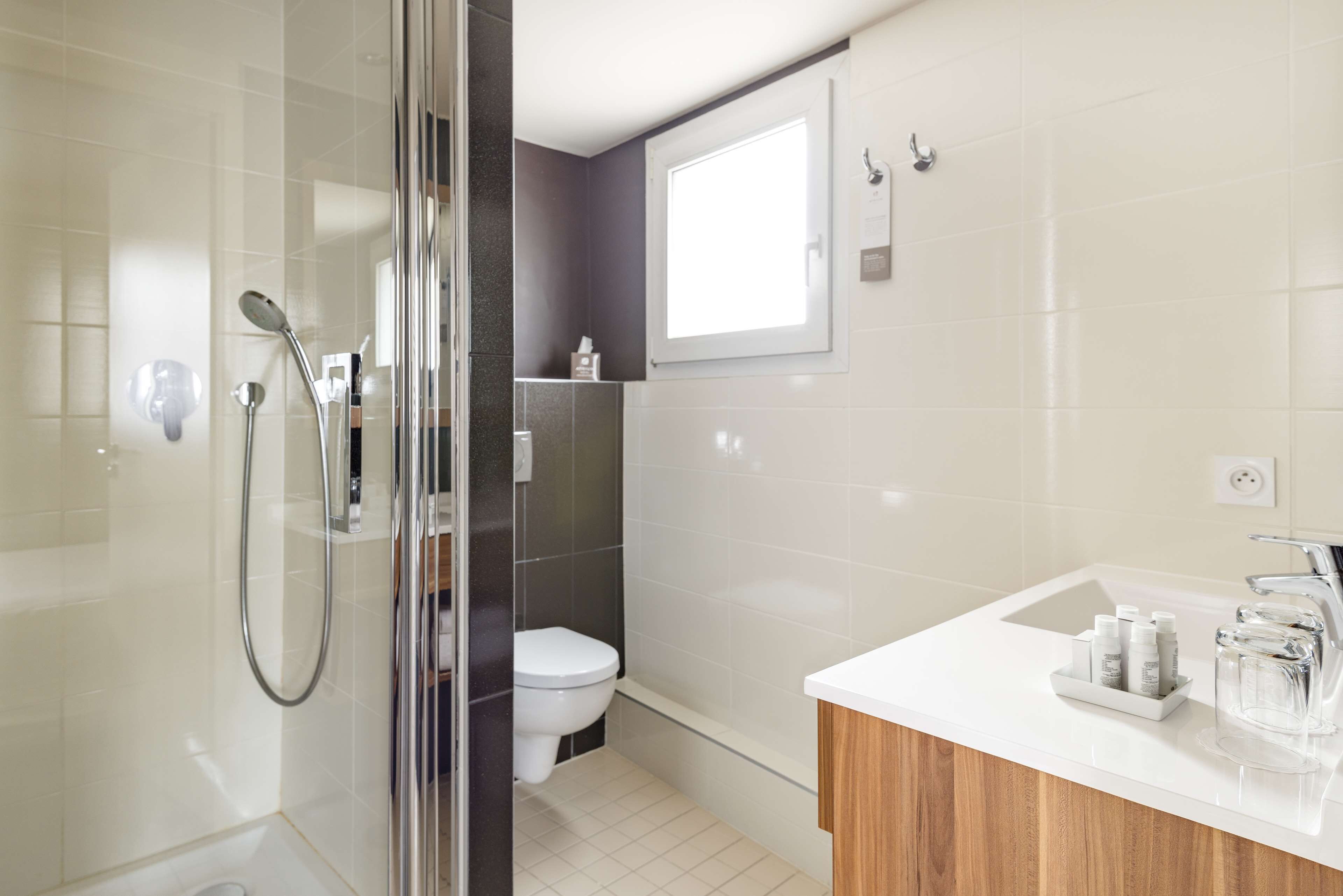Une salle de bain moderne avec une douche à l’italienne en verre, des toilettes blanches et un lavabo blanc avec un meuble-vasque en bois.