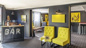 A modern bar area with a counter labeled "BAR," yellow upholstered chairs, and artwork on the walls.