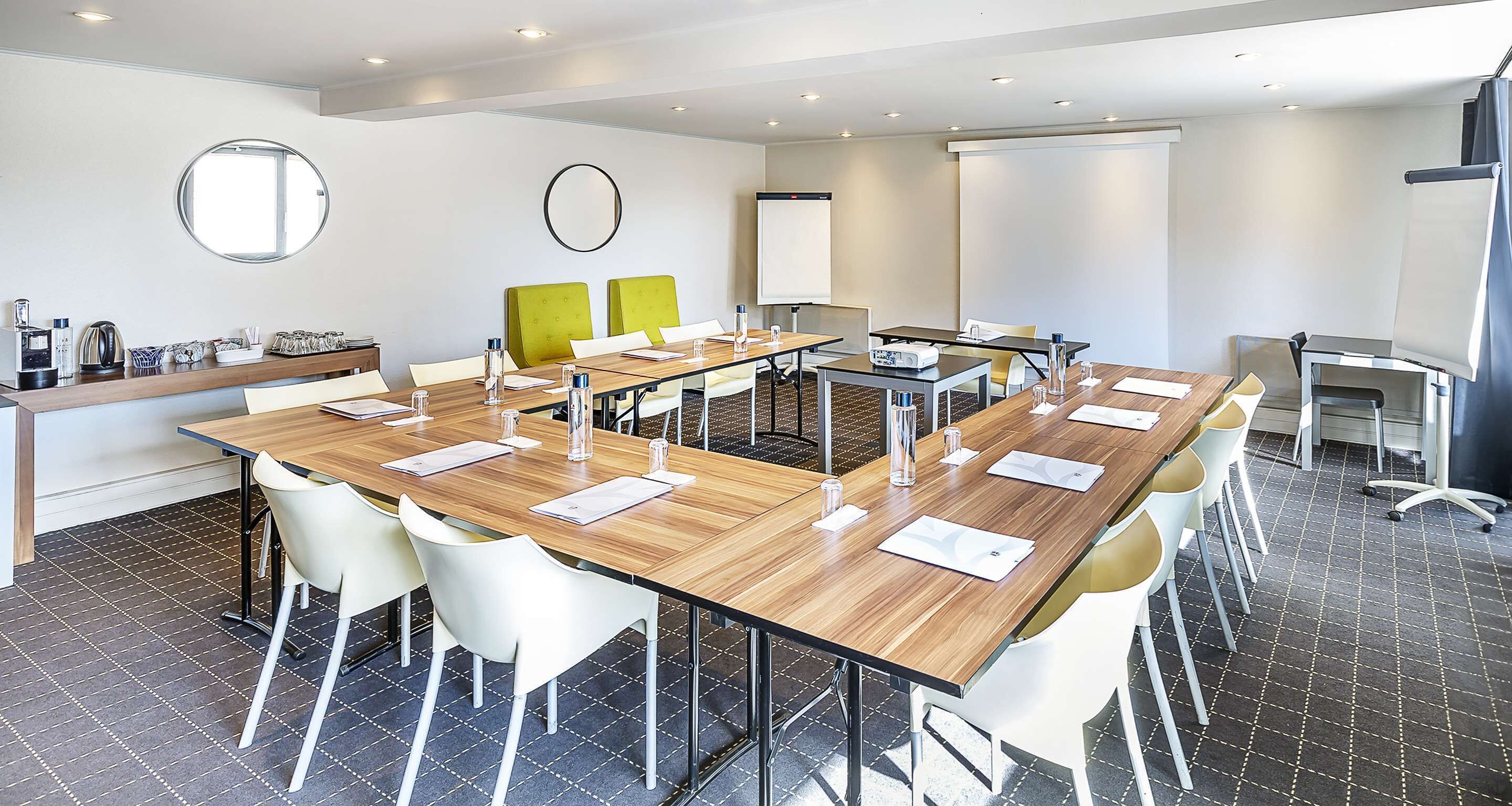 A modern conference room with a long table, white chairs, and a projector screen.