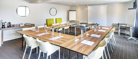 A modern conference room with a long table, white chairs, and a projector screen.