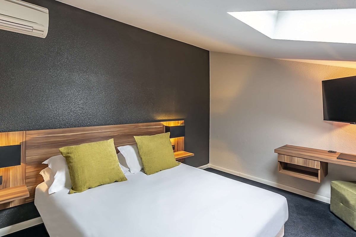 A hotel room with a bed, a desk, a TV, and a window.