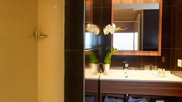 A modern bathroom with a shower, a sink with a mirror, and a vase with a flower.