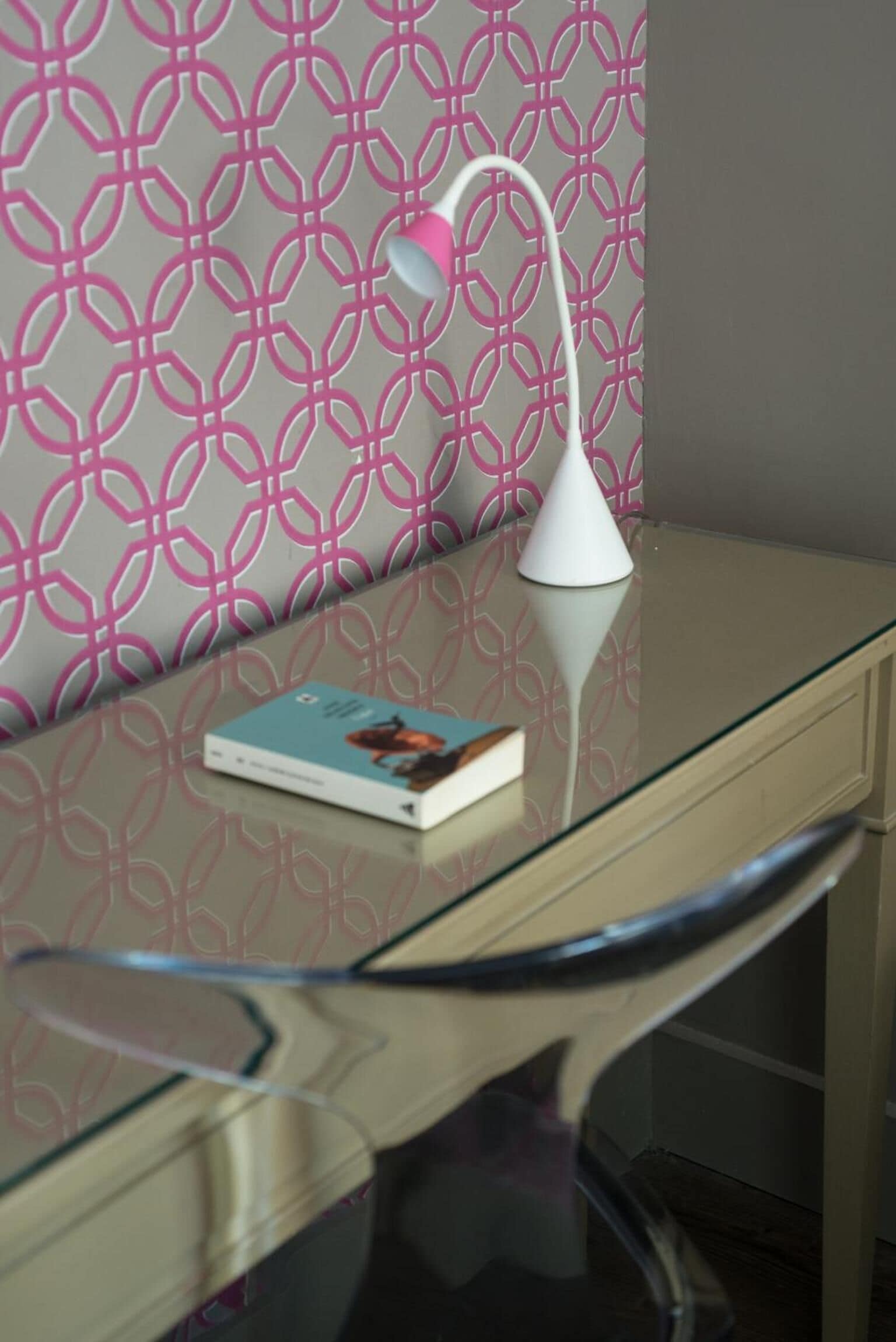 A glass desk with a book and a white lamp.