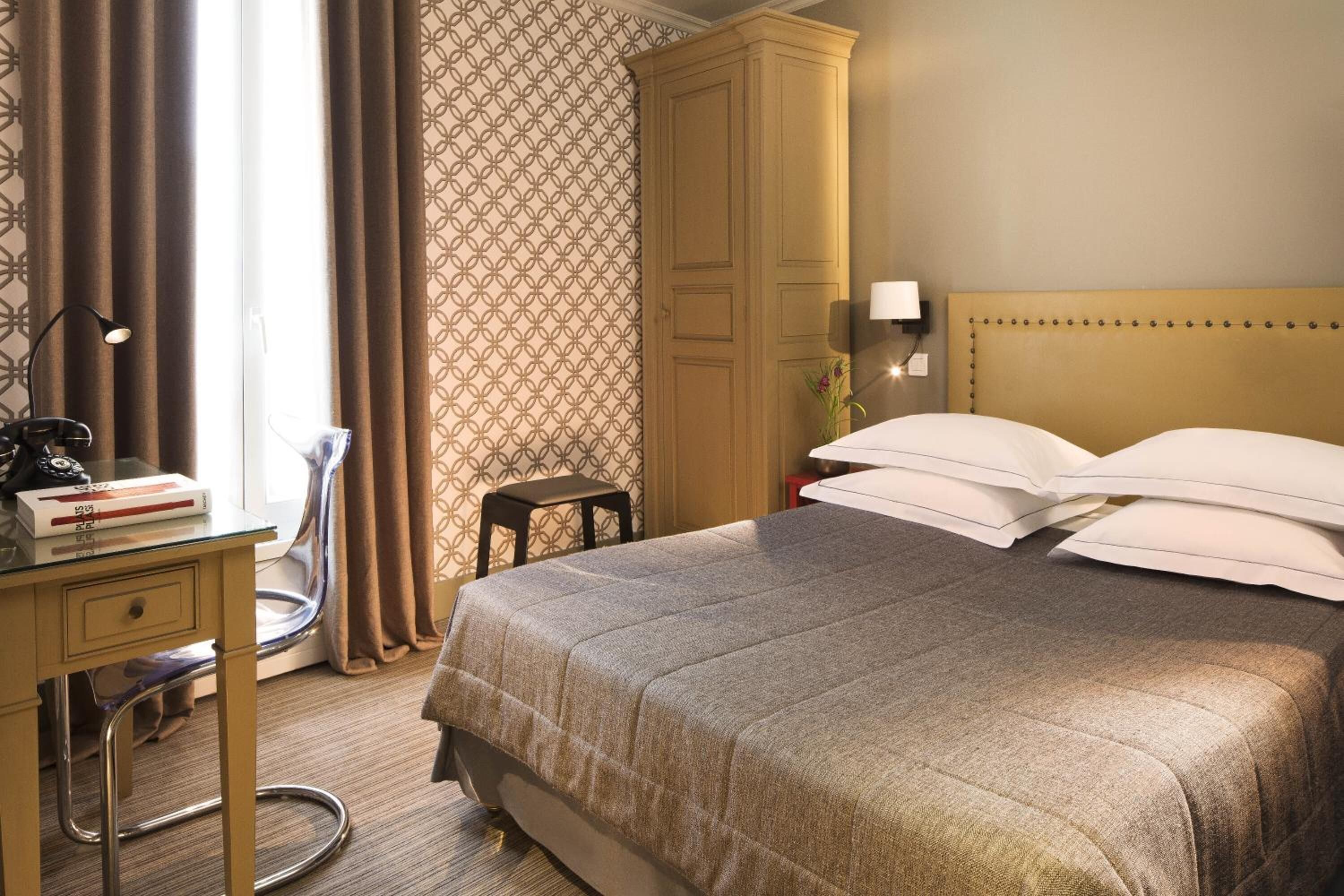 Una habitación de hotel con cama, escritorio con lámpara, una silla y un armario.