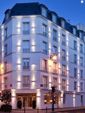 A multi-story hotel with illuminated windows and balconies, featuring a classic architectural style. - Hôtel Apollon Montparnasse (Paris)