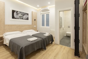 A hotel room with two beds, a wooden headboard, a framed picture on the wall, and a bathroom visible through an open door. - Hostal The Good Rooms (Madrid)