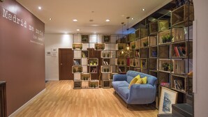 A modern hotel lobby with a wooden floor, a blue sofa with yellow cushions, and a bookshelf filled with plants and books. - Hostal The Good Rooms (Madrid)