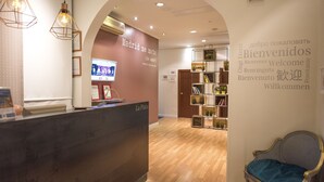 A reception area with a wooden reception desk, a TV screen, and a wall with multilingual welcome signs. - Hostal The Good Rooms (Madrid)