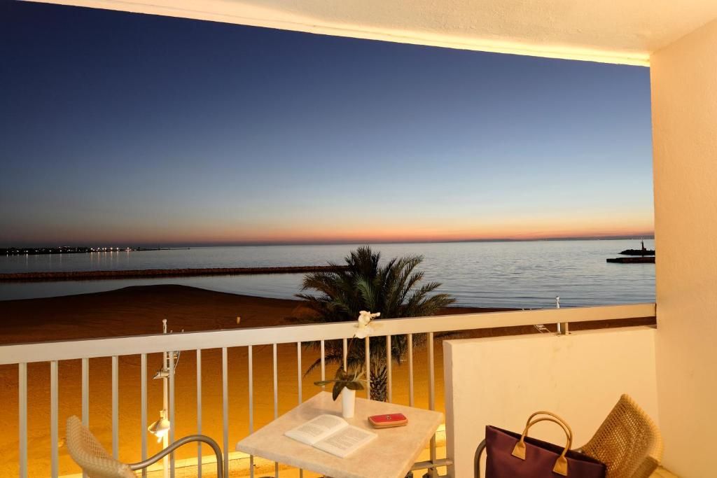 A balcony with a view of the sea at sunset, a table with a book and a red object, and a chair.