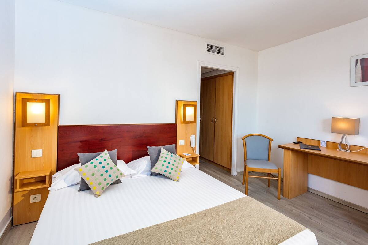 A hotel room with a large bed, two bedside tables, a desk, a chair, and a wardrobe.