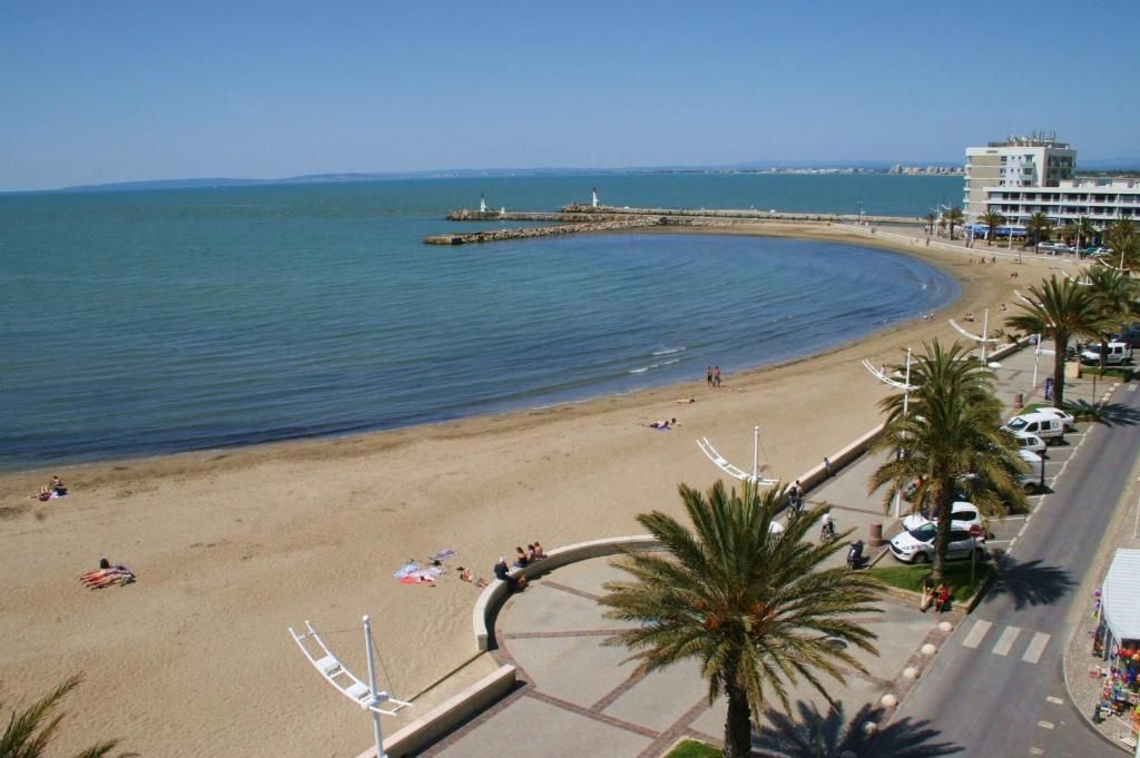 Ein Strand mit gewellter Küstenlinie, Palmen und einem Gebäude mit Balkonen mit Blick aufs Meer.