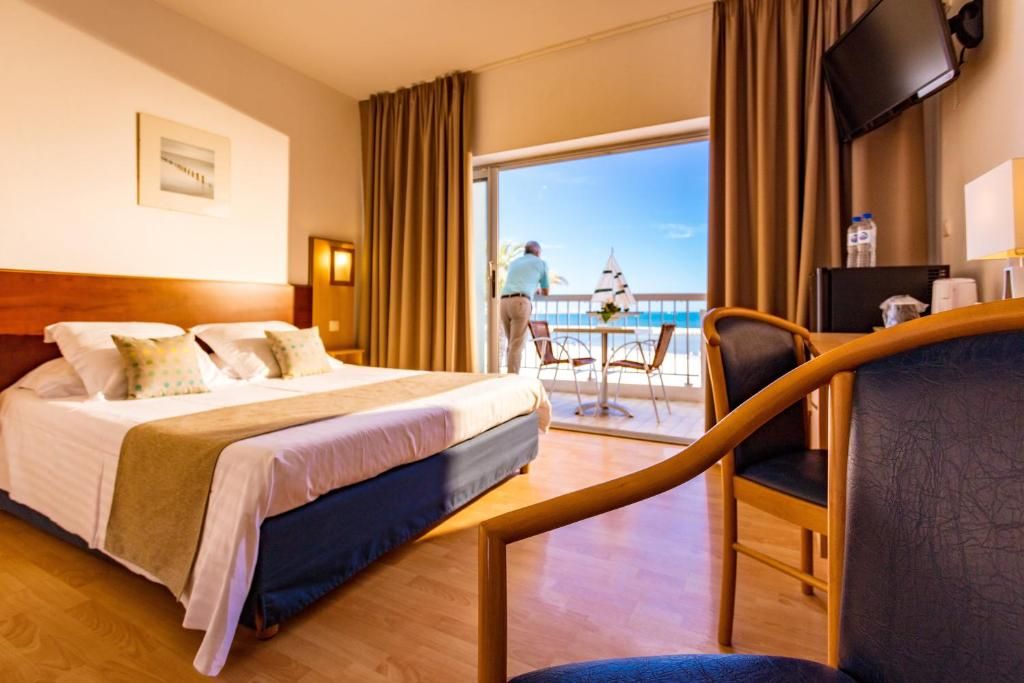 Ein Hotelzimmer mit Bett, Schreibtisch, Stuhl, Fernseher und einem Balkon mit Blick.