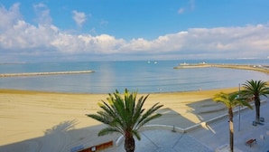 A beach with clear skies, calm water, and a few boats. There are palm trees and a paved walkway along the shore. - Splendid Hôtel Camargue (Le Grau-Du-Roi)