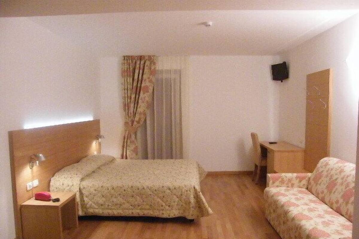 A hotel room with a bed, a desk, a chair, and a sofa.