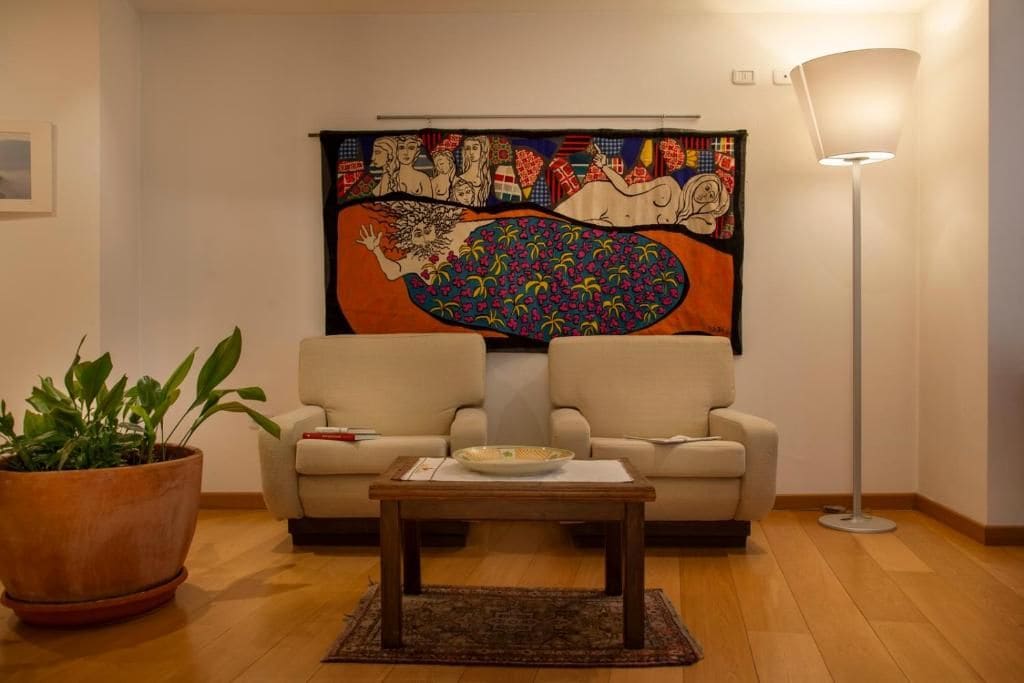 A living room with a sofa, a coffee table, a floor lamp, and a large tapestry on the wall.