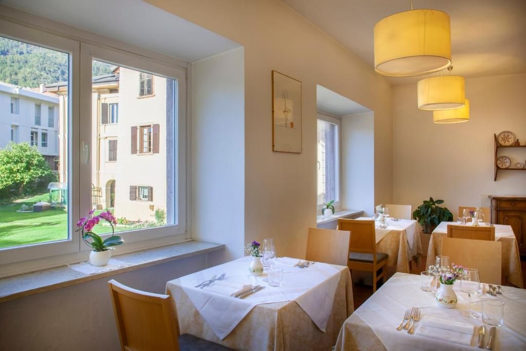 Comedor con mesas dispuestas para dos, ventana con vistas a edificios y una lámpara colgante.