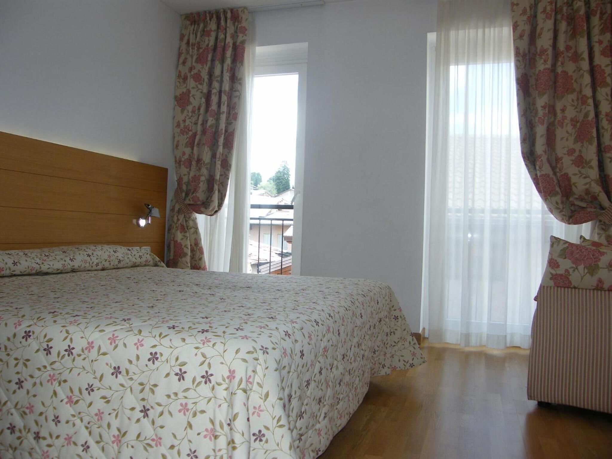 A bedroom with a bed, wooden headboard, floral curtains, and a view of a balcony.
