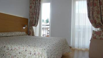 A bedroom with a bed, wooden headboard, floral curtains, and a view of a balcony.