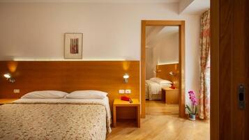 A hotel room with a wooden headboard, a bed with white linens, a bedside table with a lamp, and a mirror reflecting the room.