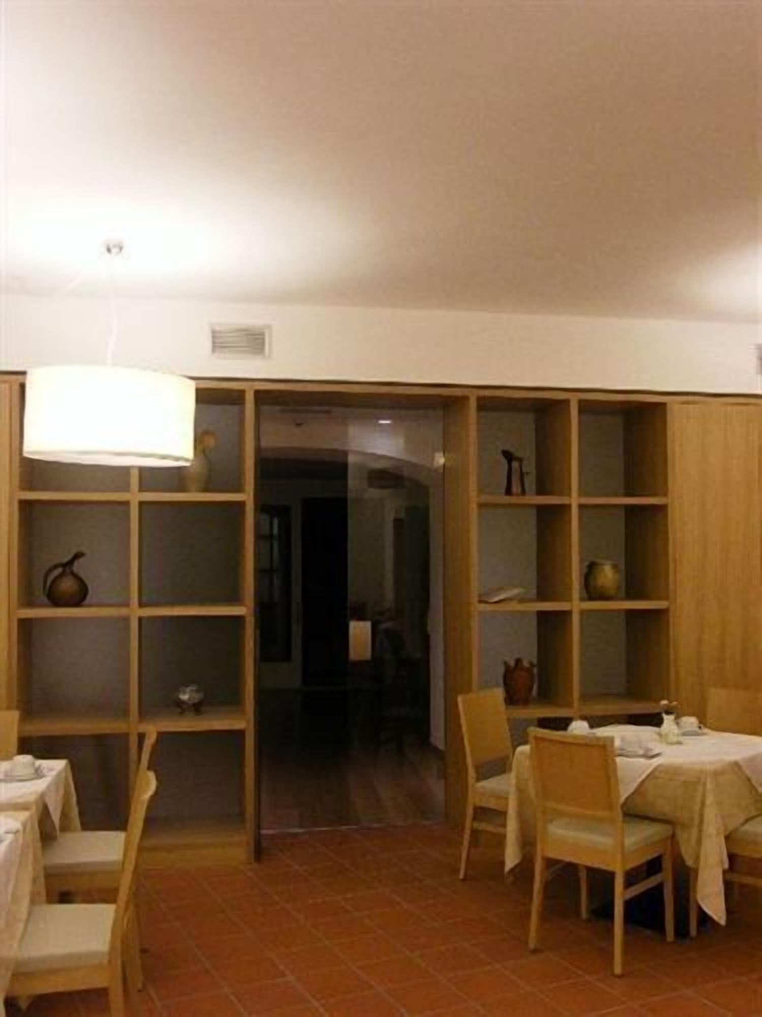 A dining area with wooden chairs and tables, a tiled floor, and a bookshelf with various items.