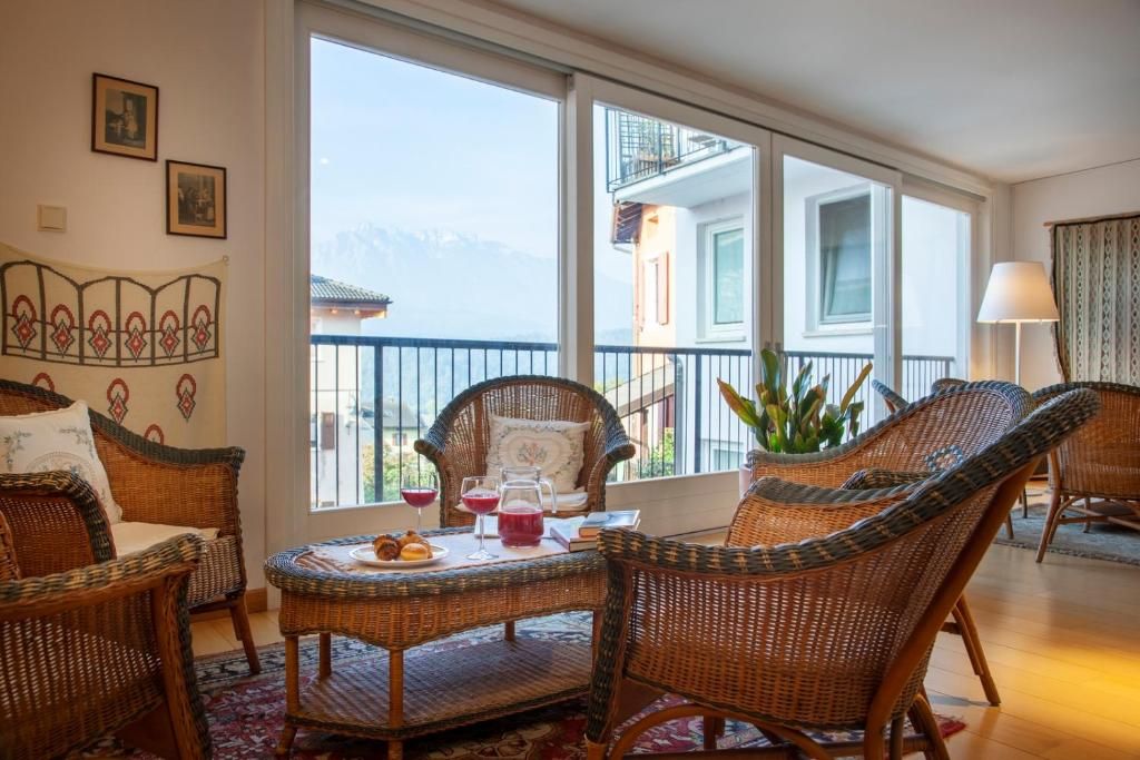 A room with wicker furniture, a dining table with a red drink, and a view of mountains through large windows.