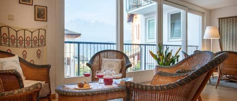 Una habitación con muebles de mimbre, una mesa de comedor con una bebida roja y vistas a montañas a través de amplios ventanales.