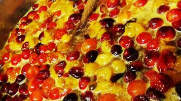 A large pot with a wooden spoon, containing a mixture of red and yellow fruits, possibly cherries and apricots, being cooked or mixed.